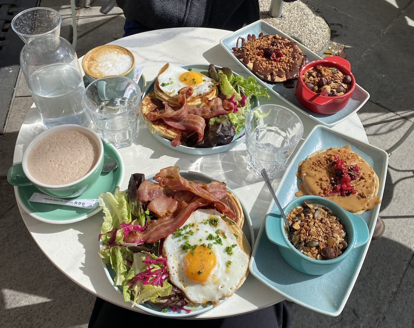 Table généreuse de brunch avec pancakes, granola bowl, café et thé glacé en terrasse